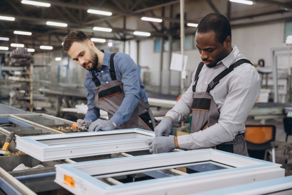Two factory workers concentrating on assembling PVC window frames on a production line in a modern manufacturing facility